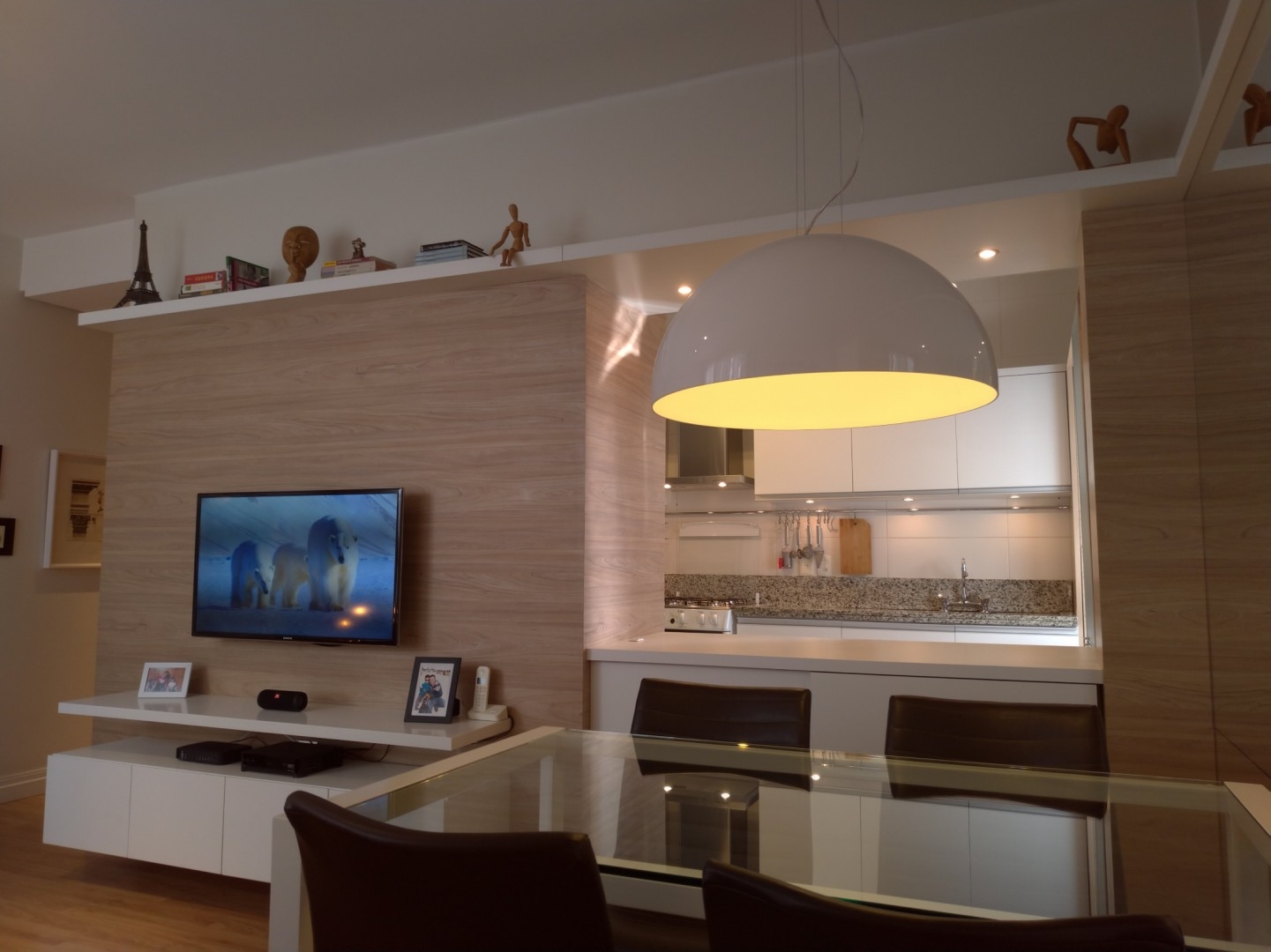 integração entre cozinha e sala feita por vão aberto na parede. TV no painel e prateleira superior. Pé-direito alto decoração design e arquitetura de interiores 