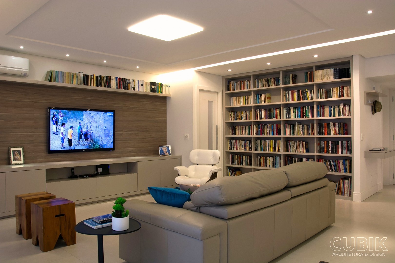 Sala de Estar, Living Contemporâneo, sanca de luz, TV LED no painel, sofá couro, estante livros, laca fosca, Porcelanato Portinari Crema Valencia, puff em madeira peroba rosa